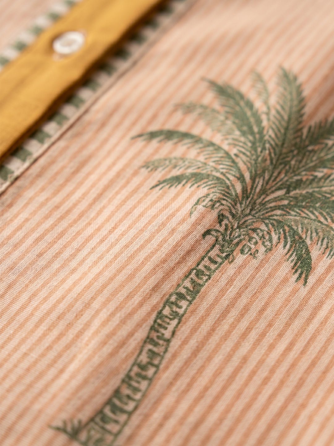 Close-up of a tan striped shirt featuring a green palm tree print and button detail.