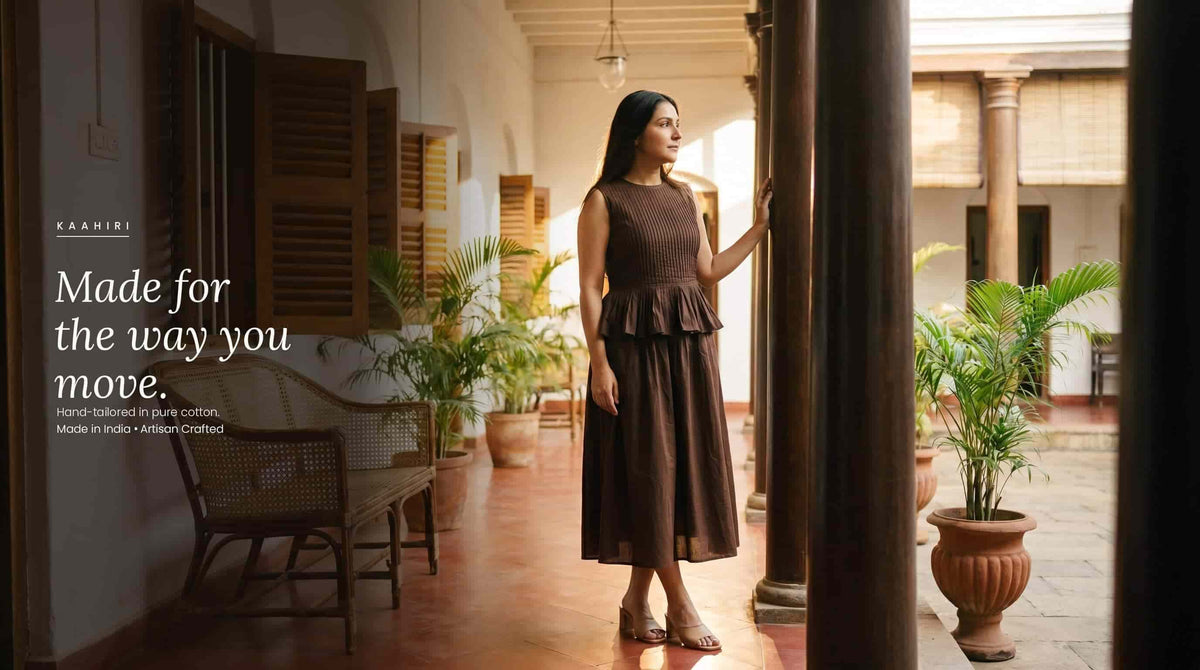Woman wearing a brown cotton peplum dress standing in a traditional Indian courtyard.