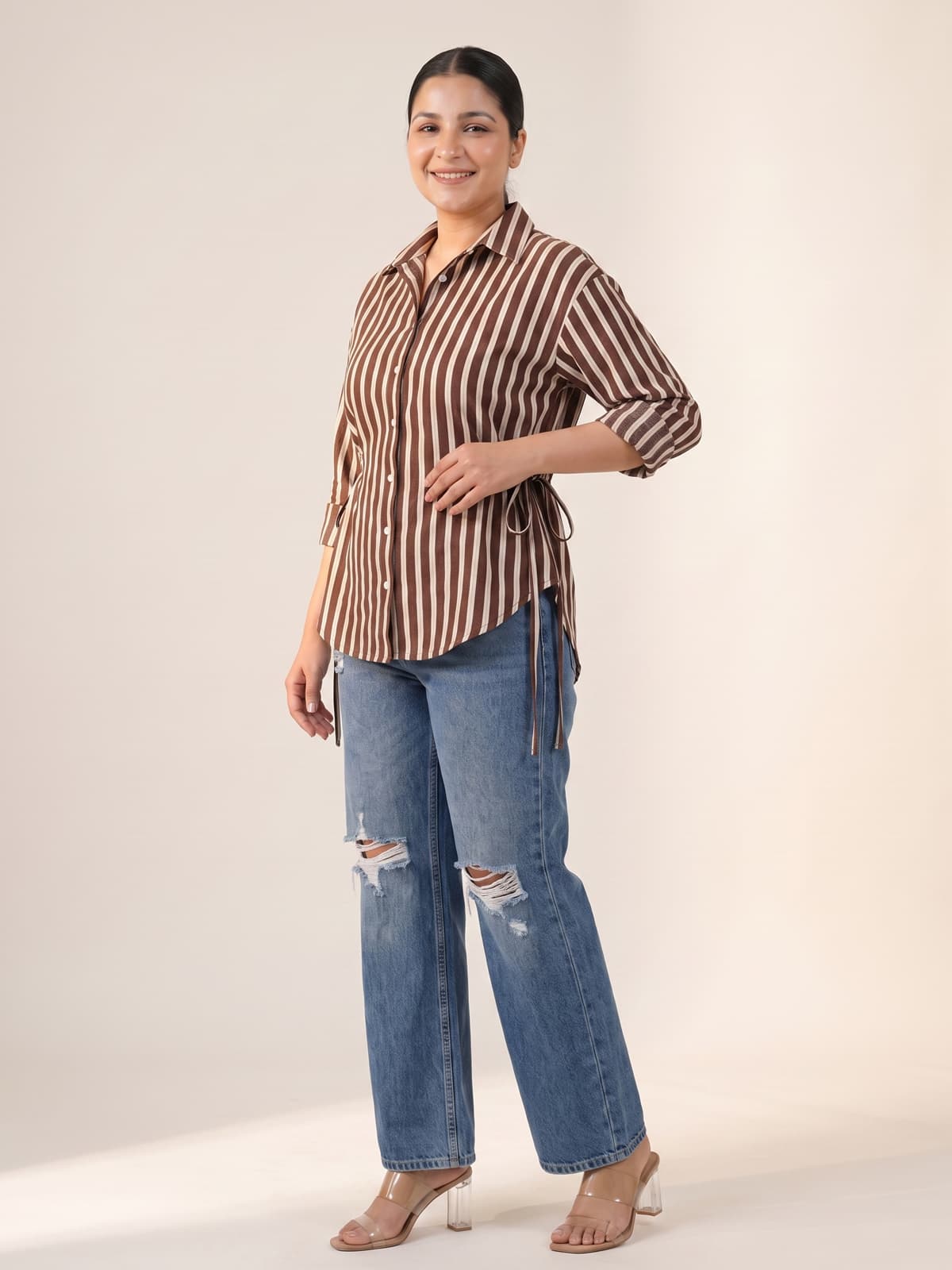 Plus size woman wearing a brown striped button-down shirt and ripped blue denim jeans