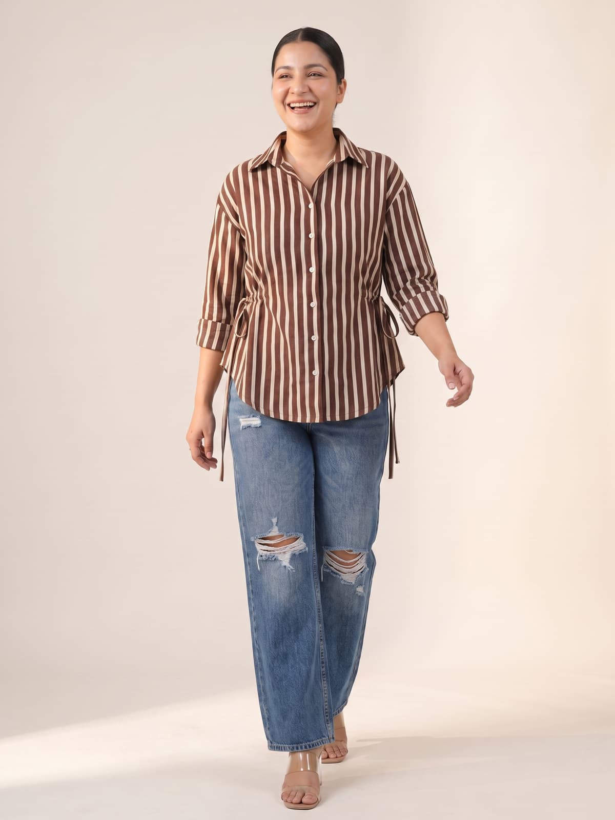 Plus size woman wearing a brown striped shirt and distressed blue jeans.