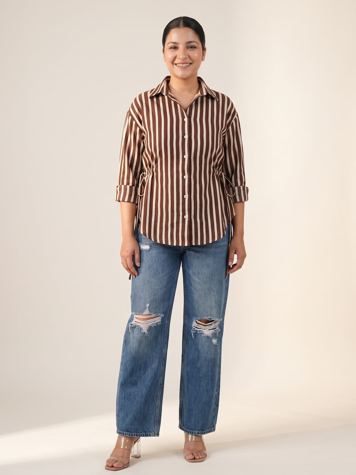 Woman wearing a brown and white striped shirt paired with ripped blue wide-leg jeans.