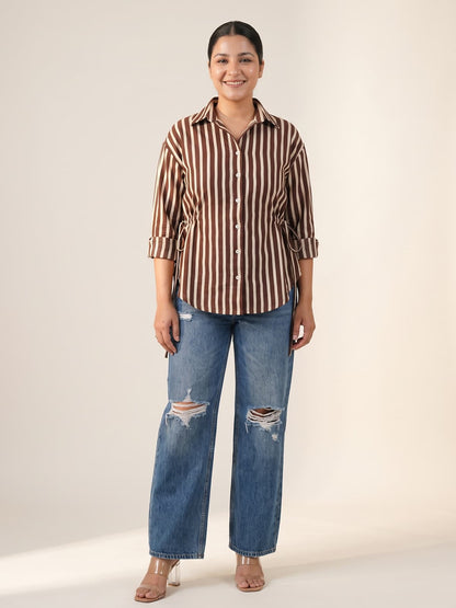 Woman wearing a brown and white striped shirt paired with ripped blue wide-leg jeans.