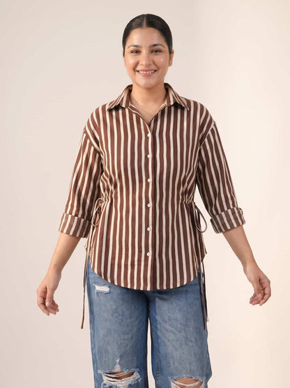 Woman wearing a brown and white striped button-down shirt and distressed blue jeans.