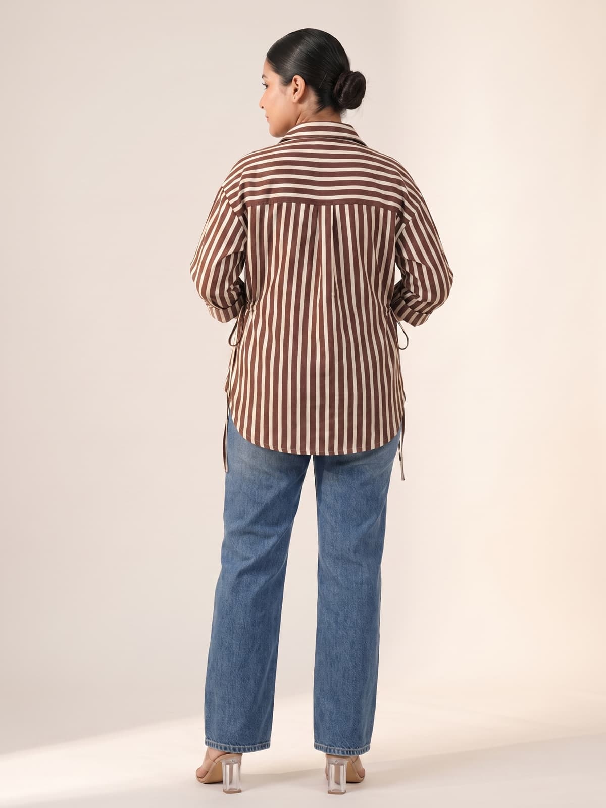 Woman from behind wearing a brown and white striped shirt and blue jeans.