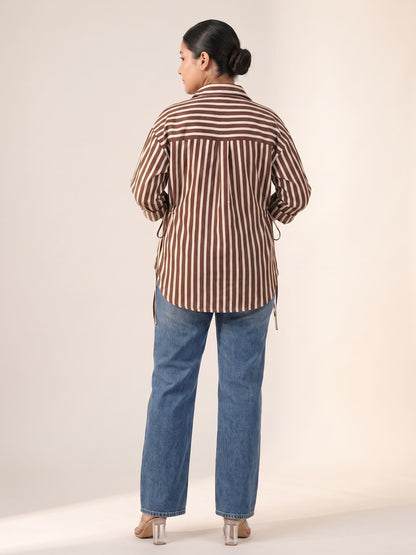 Woman from behind wearing a brown and white striped shirt and blue jeans.