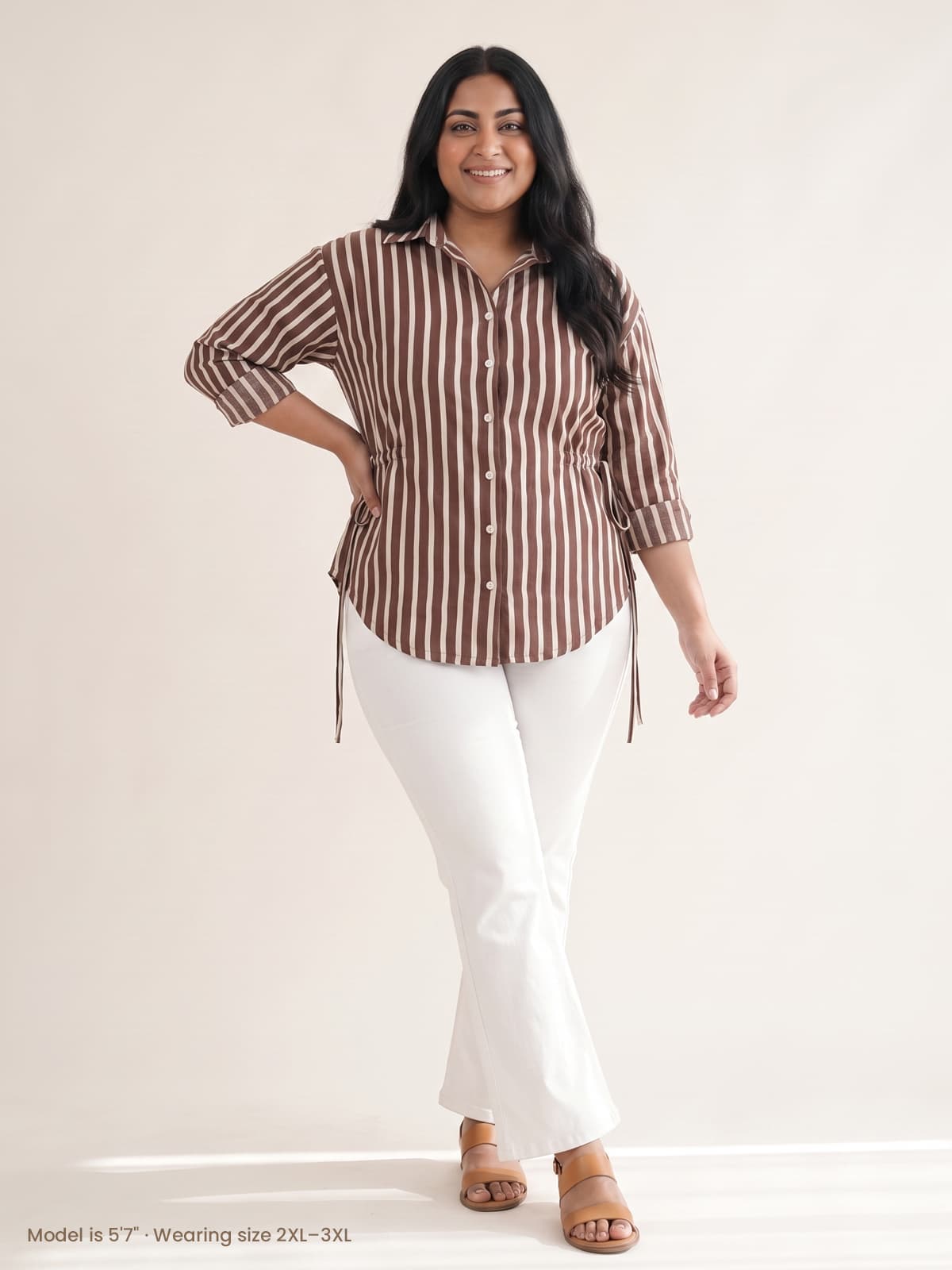 Plus size woman wearing a brown and white striped button-down shirt and white flare pants